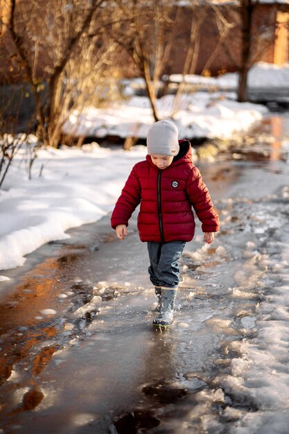 a little boy walks through the puddles among the snow