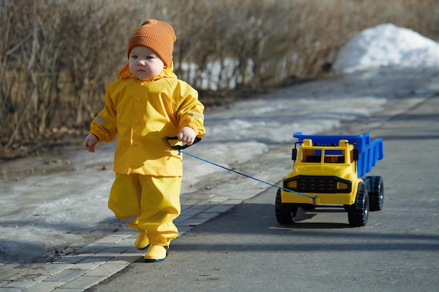 A little boy walks with a dump truck on the street