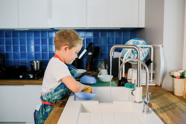 a little boy washes dishes in a modern kitchen.