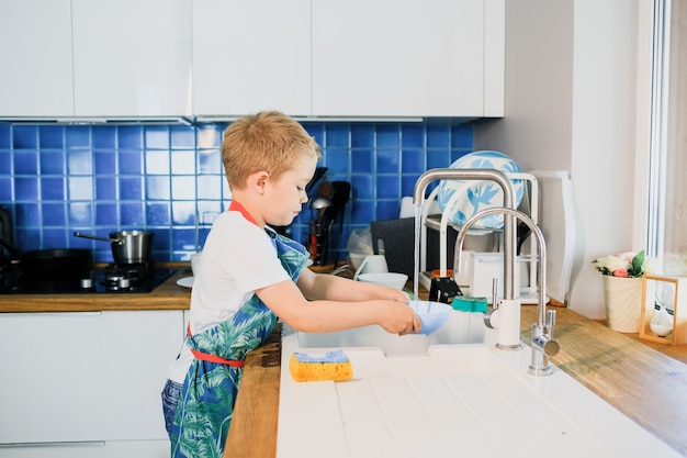 A little boy washes dishes in a modern kitchen.