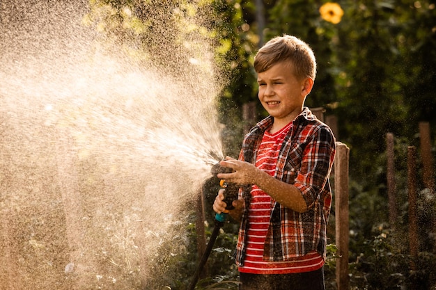 小さな男の子は植物に水をまき、大きな水しぶきを上げます