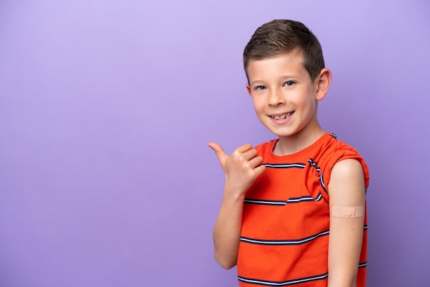 제품을 제시하기 위해 측면을 가리키는 보라색 배경에 격리된 반창고를 착용한 어린 소년