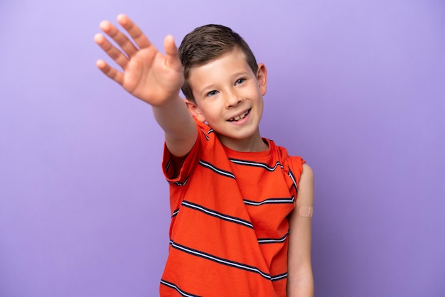 Little boy wearing a band aid isolated on purple background saluting with hand with happy expression