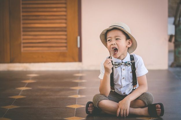 Little boy wearing hat sit on floor eating chocolate beside little bride, toned photo