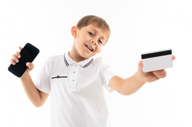 A little boy in a white shirt, blue shorts with blonde hair, black glasses with phone and card is smiling