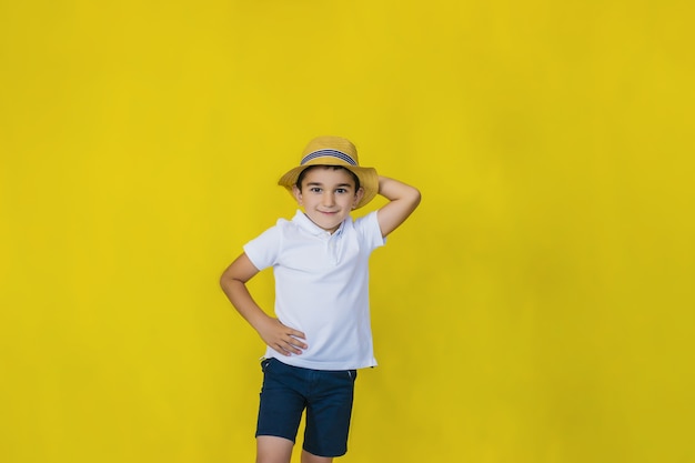 a little boy in a white shirt and straw hat on a yellow wall.