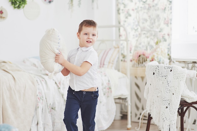 Маленький мальчик в белой рубашке с подушкой. Драка подушками