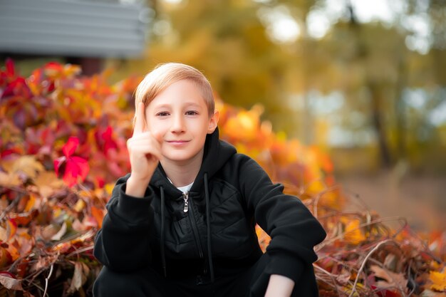 A little boy who is in a beautiful autumn park shows his thumbs up.