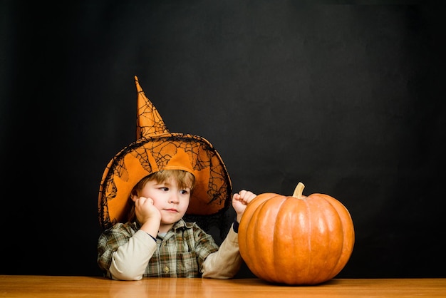 Маленький мальчик в шляпе ведьмы с тыквой хэллоуина. Джек о фонарь. Подготовка к Хэллоуину. Мальчик в костюме трюк или угощение. Ребенок с тыквой. Праздники Хэллоуина. Кошелек или жизнь. Счастливого Хэллоуина.