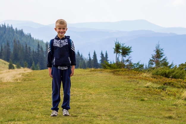 Little boy with a backpack hiking in scenic summer green carpathian mountains. child standing alone enjoying landscape mountain view. active lifestyle, adventure and weekend activity concept.