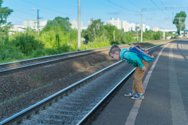 バックパックを背負った男の子が電車を待っている電車を見越してプラットフォームに一人で立っている子供