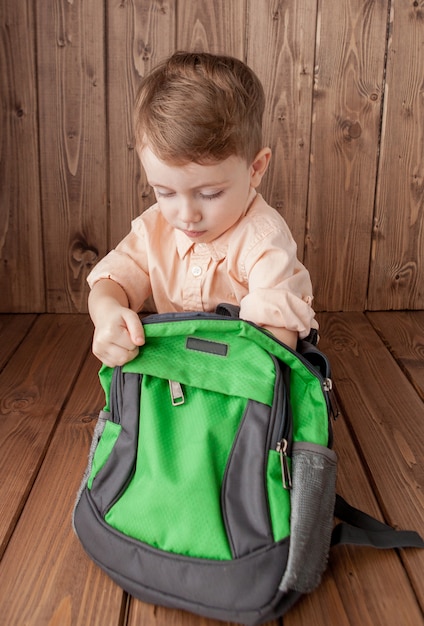 Little boy with a backpack on wooden background