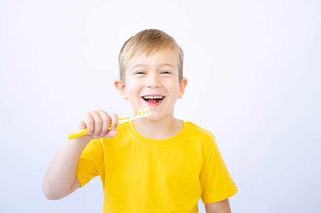 ブロンドの髪と青い目をした小さな男の子白い背景の上の子供が彼の手の分離で歯ブラシを保持している彼の歯を磨いている