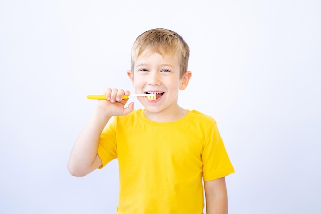 ブロンドの髪と青い目をした小さな男の子白い背景の上の子供が彼の手の分離で歯ブラシを持って歯を磨いている