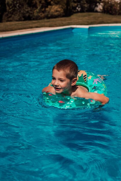 원을 가진 작은 소년은  ⁇ 은 파란 물에 목욕하고 수영장에서 수영하고 있습니다.