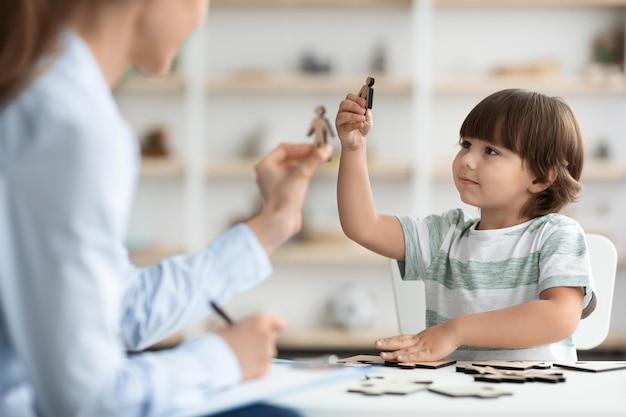 プロの子供たちと木製のフィギュアで遊ぶコミュニケーションの問題を持つ小さな男の子