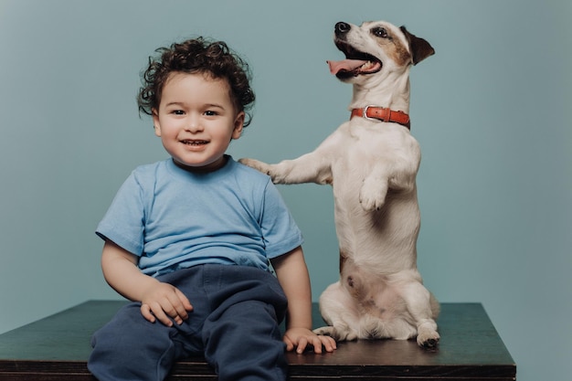 Little boy with curly hair in casual on table with dog Kid plays with pet Jack russell terrier