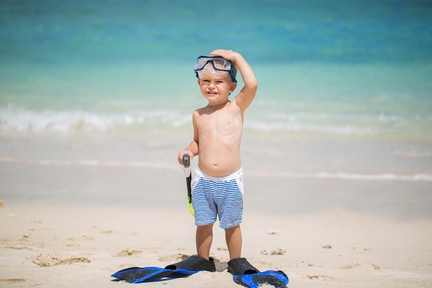Маленький мальчик с маской для подводного плавания и ластами плавать на пляже