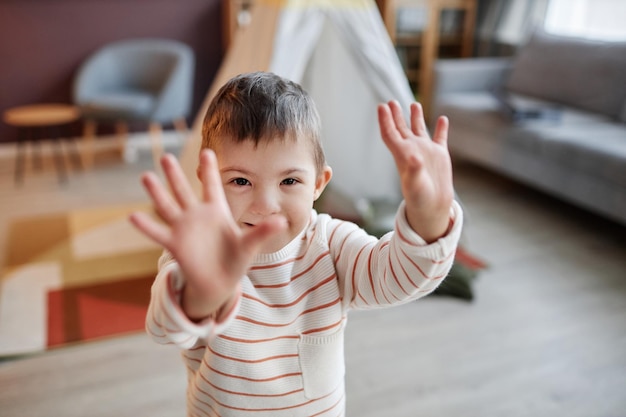 カメラに向かって手を上げるダウン症の小さな男の子