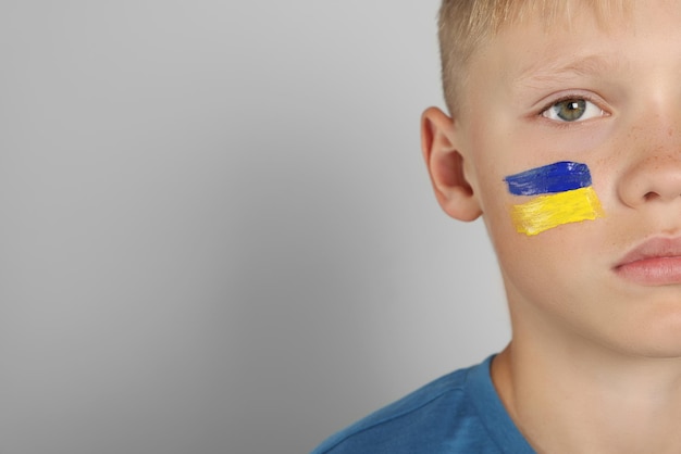 Little boy with drawing of Ukrainian flag on face against light grey background space for text