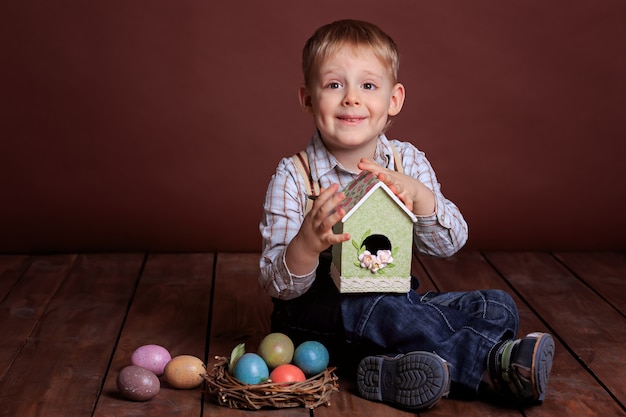 Little boy with Easter toys. Colorful easter eggs in a wicker nest, birdhouse for birds