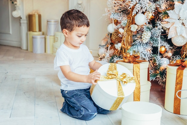 Little boy with gift box near Christmas tree at home