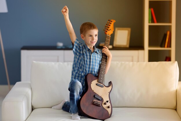 Little boy with a guitar on a sofa at home