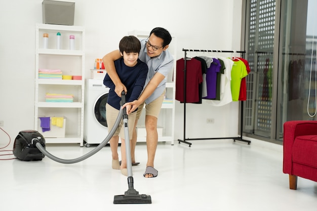 Little boy with his father use vacuuming the room. Father and son doing the cleaning in the house.