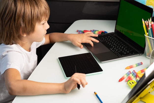 Маленький мальчик с ноутбуком и графическим планшетом зеленый хромакей на ноутбуке