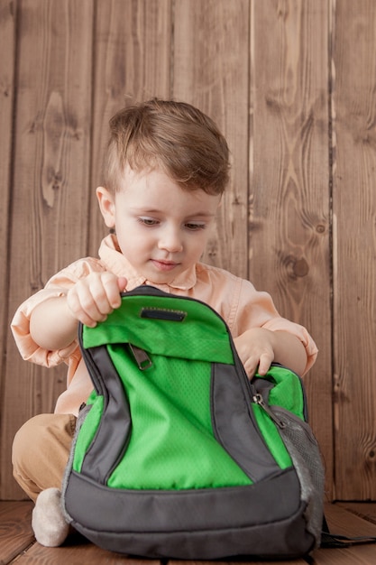 Little boy with large school bag on wooden background