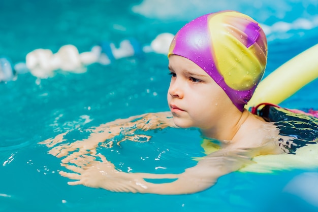 A little boy with a life jacket on his chest learns to swim in an indoor pool.