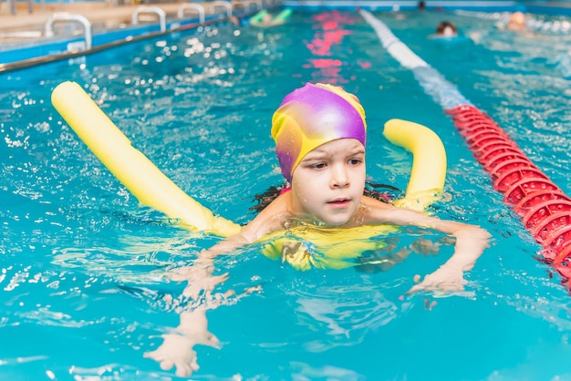 Un bambino con un giubbotto di salvataggio sul petto impara a nuotare in una piscina coperta.