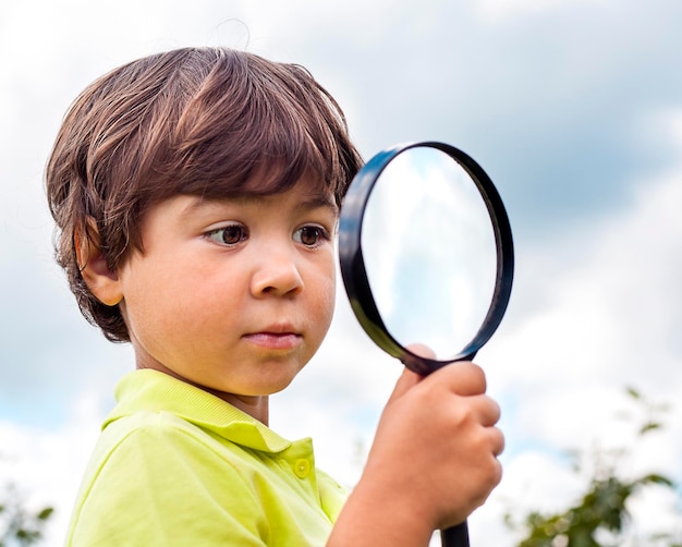 little boy with a magnifying glass in his hands close-up outdoors