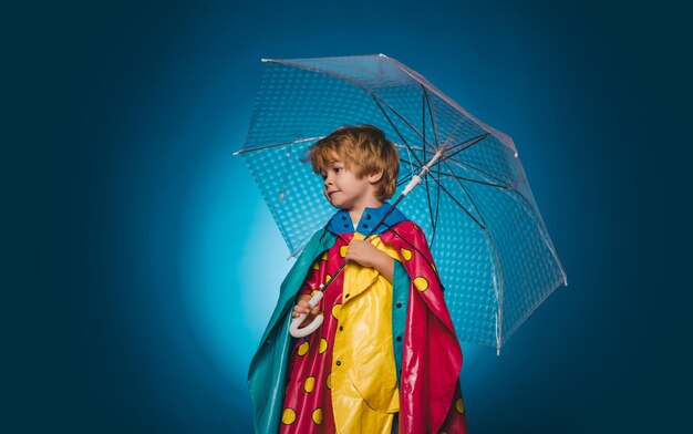 Little boy with rainbow-colored umbrella isolated on blue background. Autumn mood and the weather are warm and sunny and rain is possible. Kid in rain. Cloud rain umbrella. Raining concept.