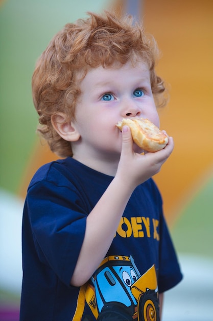 A little boy with red hair eats delicious bread