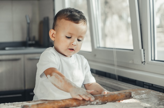 A little boy with a rolling pin in the kitchen preparing dough baking