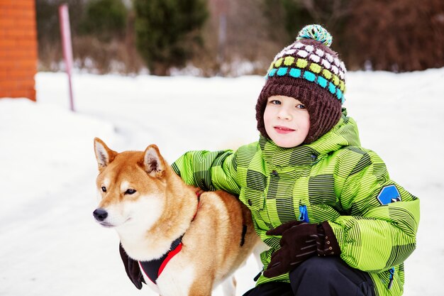 Little boy with Shiba Inu dog outdoors in the winter