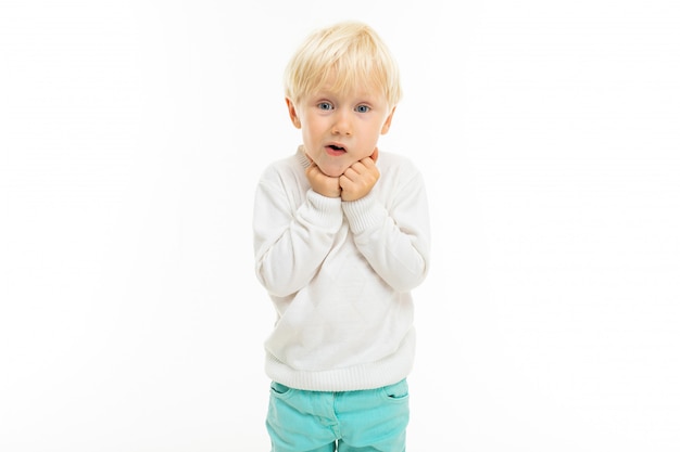 Little boy with short blonde hair, blue eyes, cute appearance, in white jacket, light blue pants, stands and is surprised