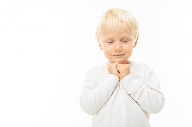 Photo little boy with short blonde hair, blue eyes, cute appearance, in white jacket, light blue pants, stands and quietly laid hands