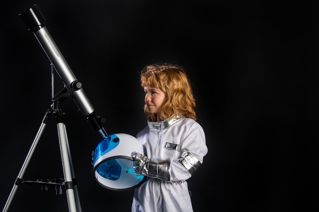 A little boy with telescope and space helmet dreams of becoming an astronaut and flying into space c