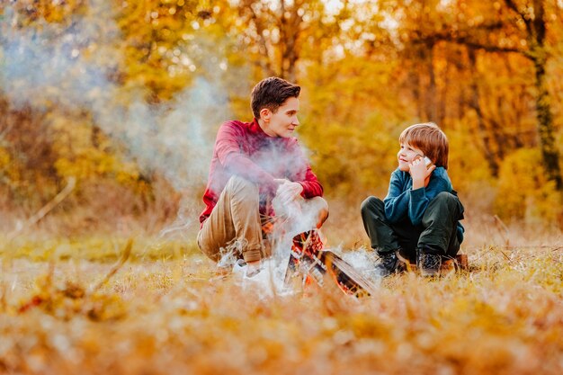 A little boy and a woman with a short haircut of androgynous\
appearance are sitting in the forest by the fire with iron mugs and\
talking. high quality 4k footage