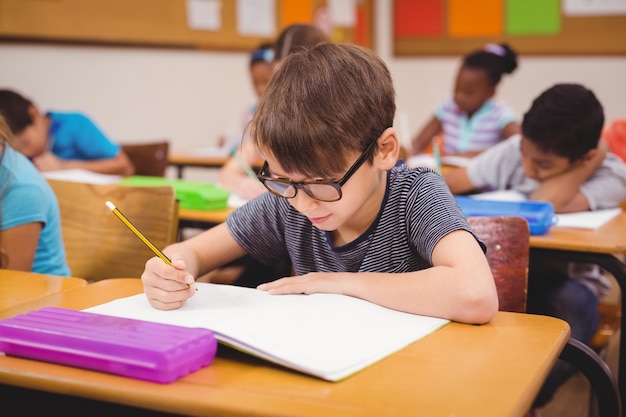 彼の机の上で授業で働く小さな男の子