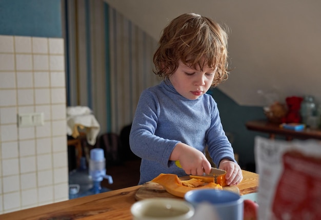 Foto un ragazzino lavora in cucina taglia una zucca