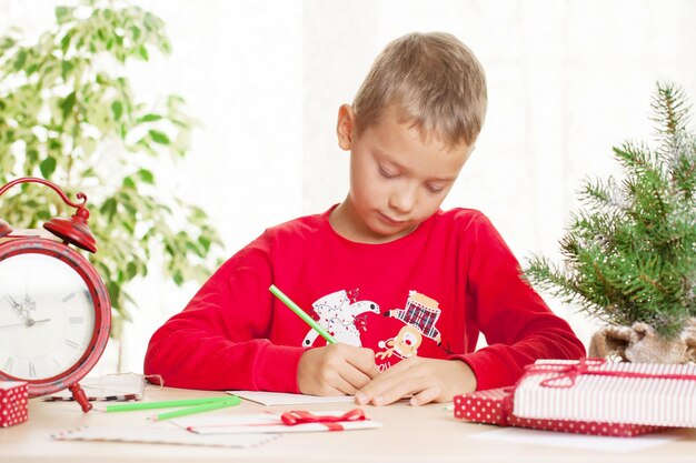 Photo little boy writes a letter to santa claus about christmas gift and wishes