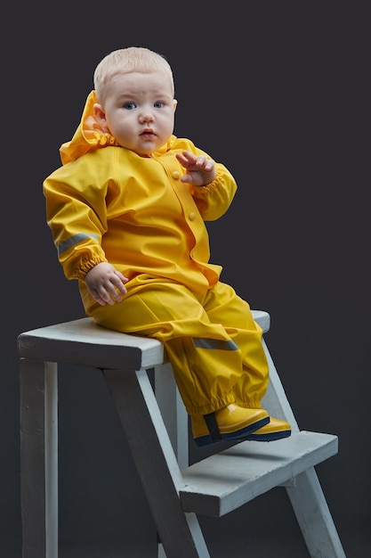 A little boy in yellow firefighter suit sits on white staircase