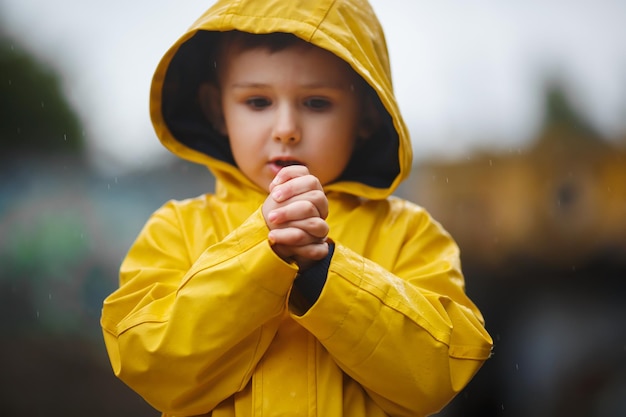 Little boy in a yellow raincoat on the street with frozen hands.