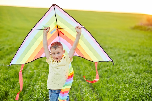 Little boy in yellow shirt running with kite in the field on summer day