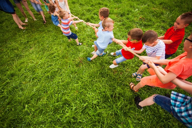 Маленькие мальчики и девочки играют в перетягивание каната в саду