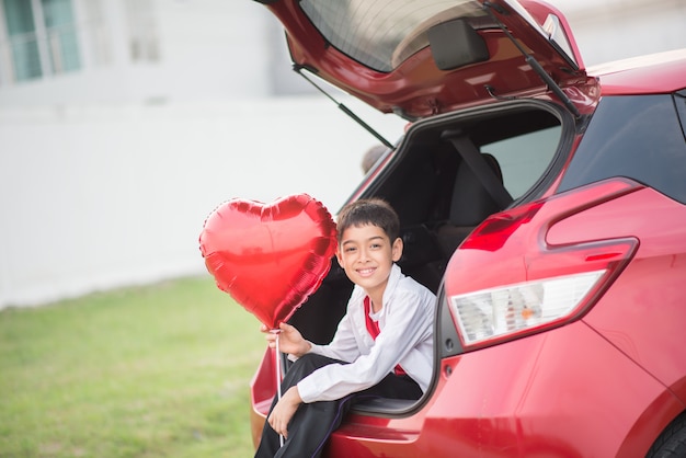 Little boys sitting on the back door of the car with balloon heart in hand