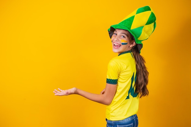 Little brazilian fan girl with her back on yellow background with brazil shirt